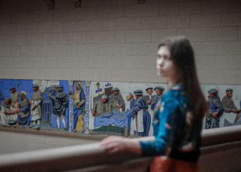 a woman standing in front of a wall with paintings on it