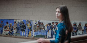 a woman standing in front of a wall with paintings on it