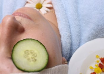 woman wearing blue robe lying with cucumber on eye
