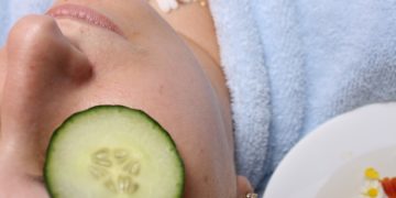 woman wearing blue robe lying with cucumber on eye