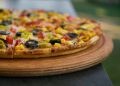 pizza with green and red berries and black berries on brown wooden round plate