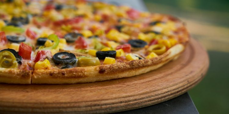 pizza with green and red berries and black berries on brown wooden round plate