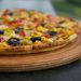 pizza with green and red berries and black berries on brown wooden round plate