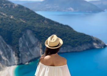 a woman in a white dress and hat looking at the ocean