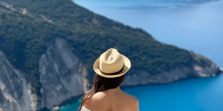 a woman in a white dress and hat looking at the ocean