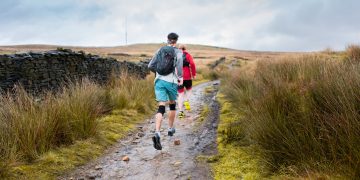 man in blue jacket walking on dirt road during daytime